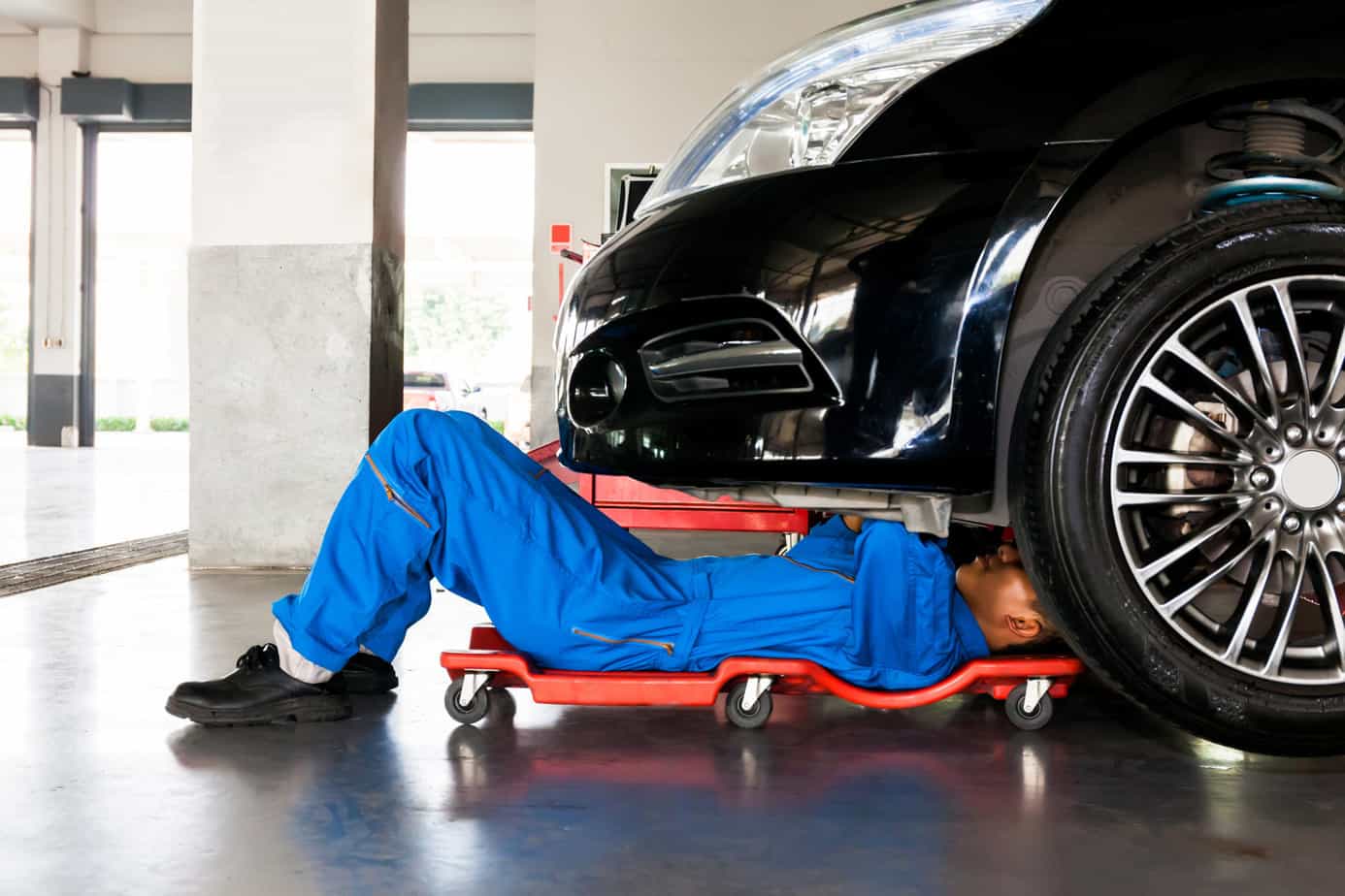 Mechanic in blue uniform lying down and working under car | Auto repair industry